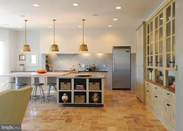 kitchen featuring pendant lighting, decorative backsplash, a breakfast bar area, and stainless steel built in fridge