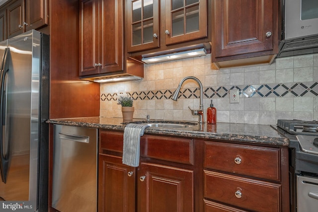 kitchen with dark stone counters, appliances with stainless steel finishes, tasteful backsplash, and sink