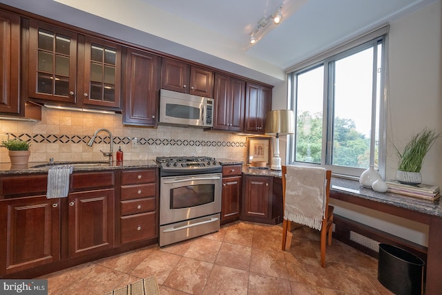 kitchen with dark stone counters, stainless steel appliances, backsplash, and sink