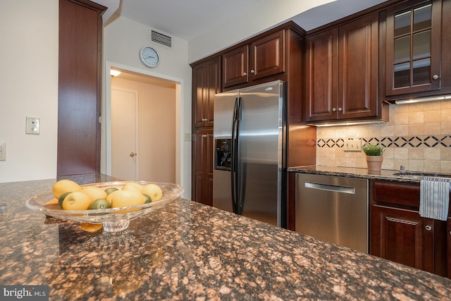 kitchen with appliances with stainless steel finishes, dark stone counters, backsplash, and dark brown cabinets