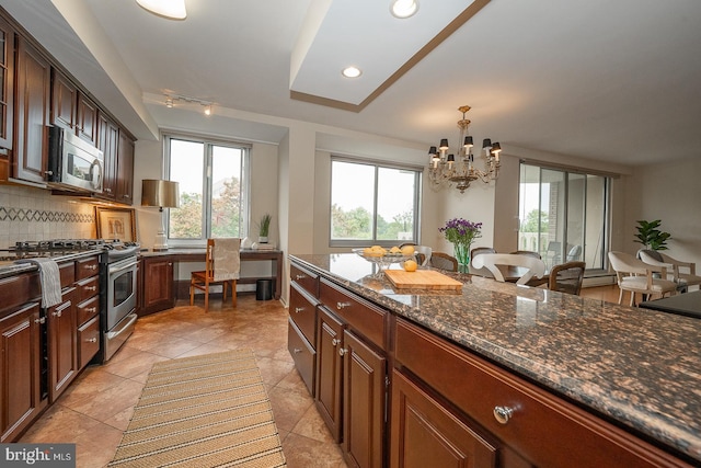 kitchen featuring appliances with stainless steel finishes, decorative backsplash, dark stone countertops, decorative light fixtures, and a notable chandelier