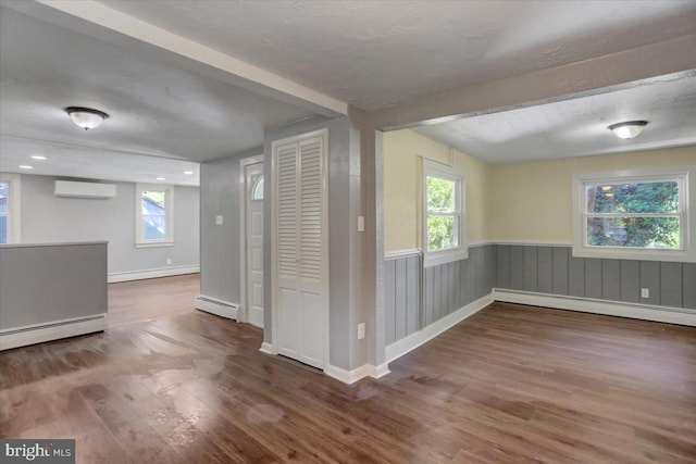 unfurnished room with a wall mounted air conditioner, a baseboard radiator, a wealth of natural light, and dark wood-type flooring