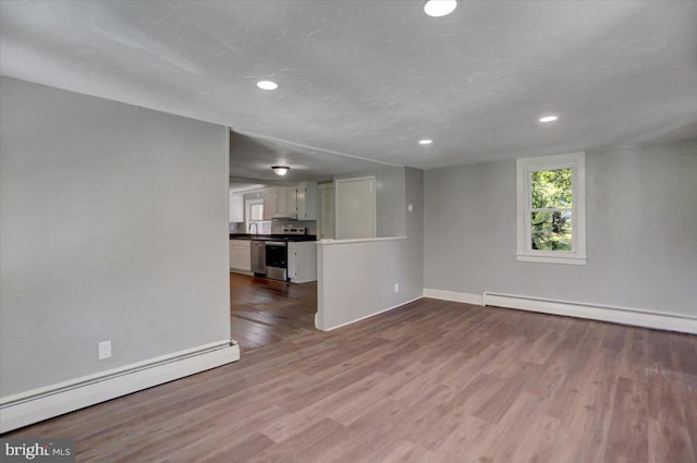 unfurnished living room with baseboard heating, sink, and light hardwood / wood-style floors