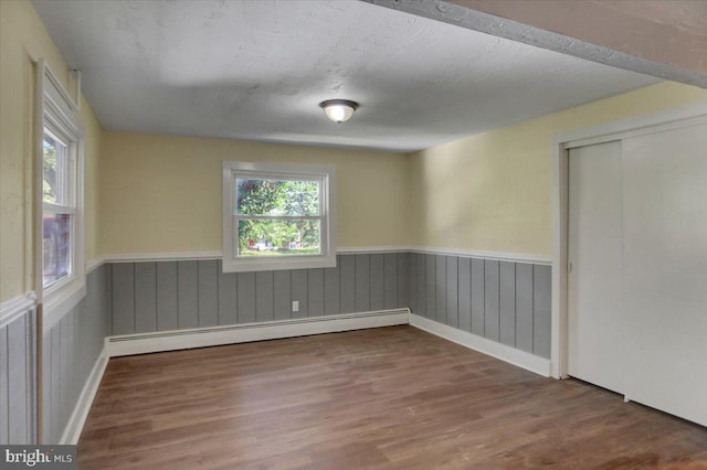 unfurnished room with hardwood / wood-style flooring, a textured ceiling, and a baseboard heating unit