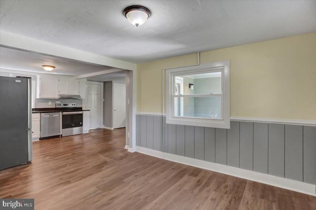 interior space with white cabinets, a textured ceiling, stainless steel appliances, and hardwood / wood-style floors