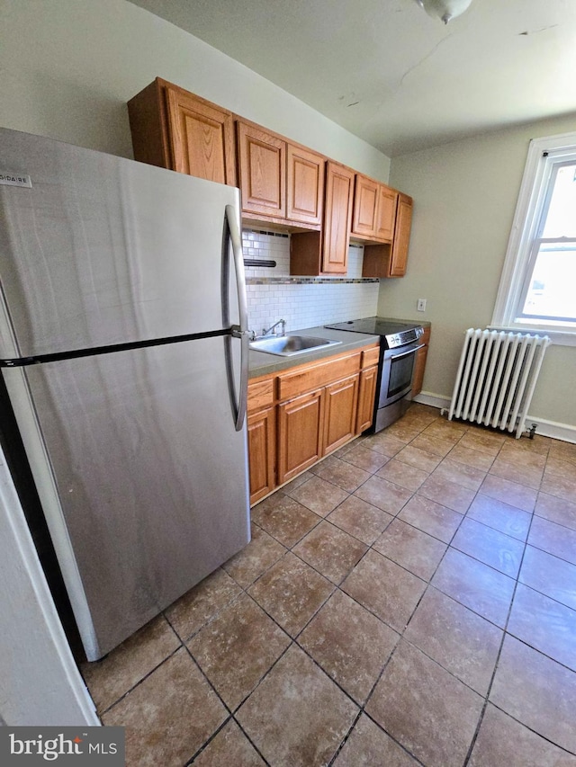 kitchen with radiator, sink, stainless steel appliances, tile patterned flooring, and backsplash