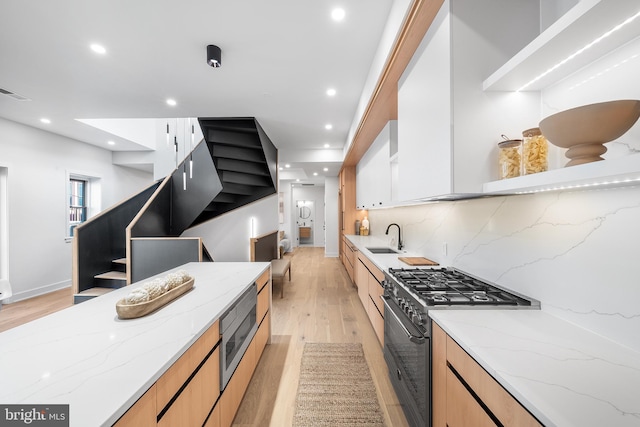 kitchen with sink, light stone counters, light hardwood / wood-style flooring, decorative backsplash, and appliances with stainless steel finishes