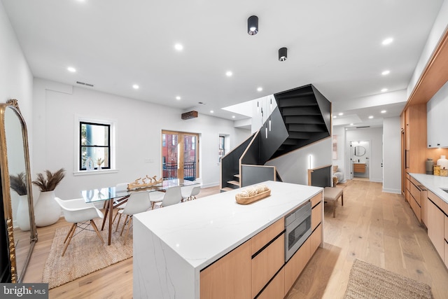 kitchen featuring stainless steel microwave, light wood-type flooring, light brown cabinetry, a large island, and light stone counters