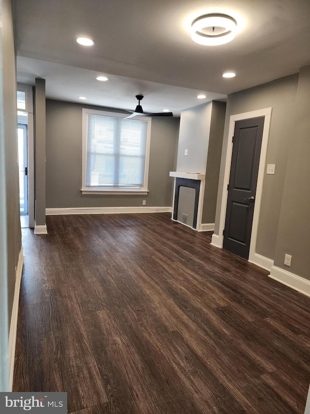 unfurnished living room with a fireplace, ceiling fan, and dark wood-type flooring