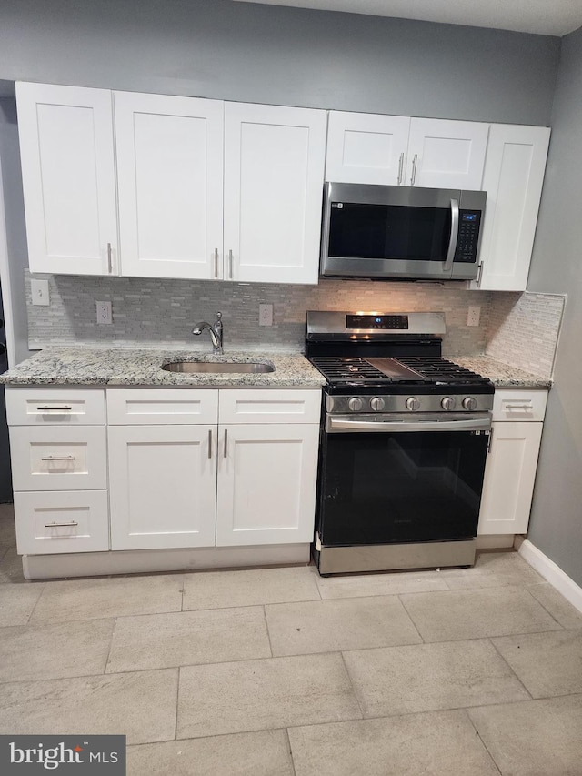 kitchen featuring light stone counters, sink, white cabinetry, stainless steel appliances, and backsplash