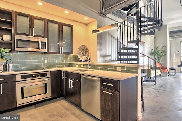 kitchen featuring kitchen peninsula, tasteful backsplash, dark brown cabinetry, stainless steel appliances, and sink