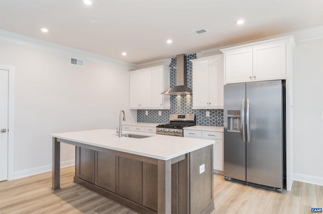 kitchen featuring white cabinets, appliances with stainless steel finishes, a kitchen island with sink, and wall chimney range hood