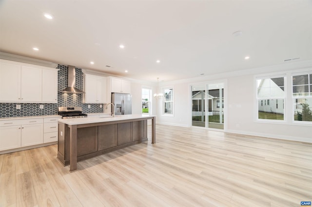 kitchen with a center island with sink, a wealth of natural light, wall chimney range hood, and appliances with stainless steel finishes