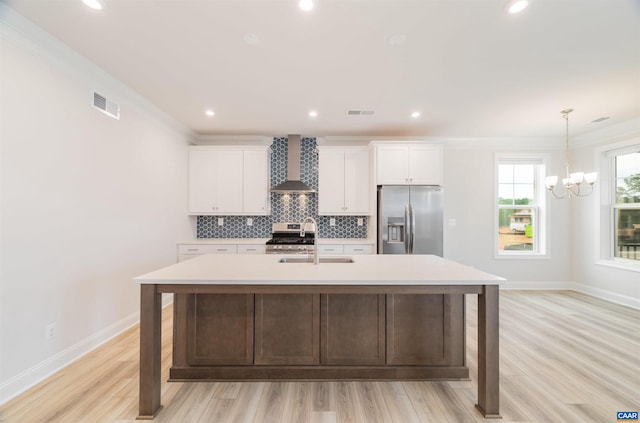 kitchen with white cabinetry, an island with sink, stainless steel appliances, and wall chimney range hood