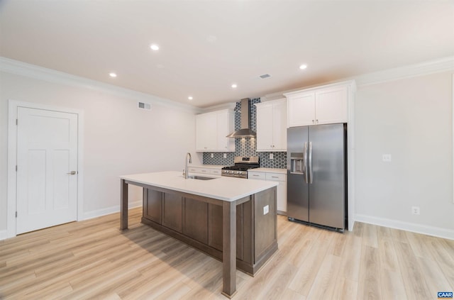 kitchen featuring appliances with stainless steel finishes, wall chimney exhaust hood, sink, white cabinetry, and an island with sink