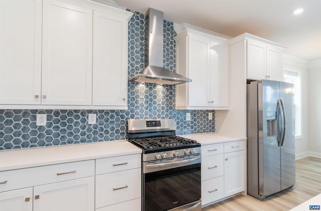 kitchen featuring tasteful backsplash, wall chimney exhaust hood, stainless steel appliances, white cabinets, and light hardwood / wood-style floors