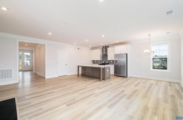 kitchen featuring a center island, wall chimney range hood, stainless steel fridge with ice dispenser, pendant lighting, and white cabinets