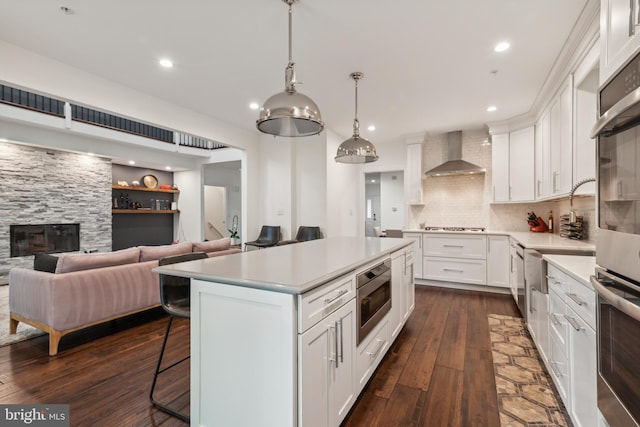 kitchen with white cabinetry, wall chimney exhaust hood, stainless steel appliances, tasteful backsplash, and a breakfast bar area