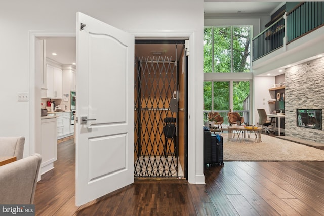 foyer with a stone fireplace, dark wood-type flooring, a high ceiling, and ornamental molding