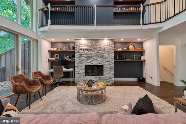 living room with built in shelves, a stone fireplace, a towering ceiling, and dark wood-type flooring