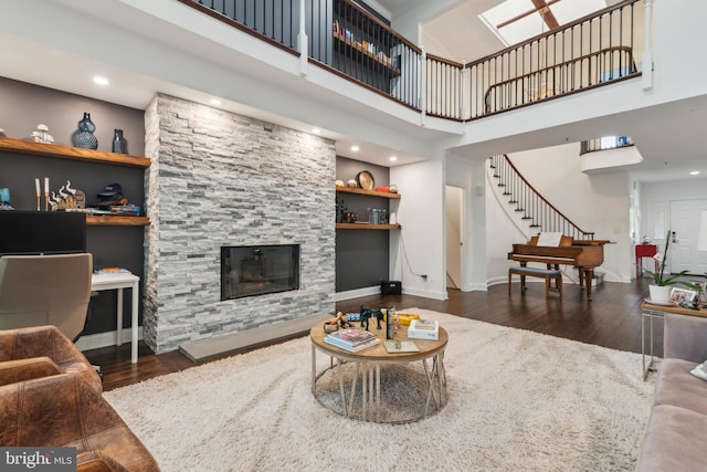 living room featuring a stone fireplace, dark hardwood / wood-style flooring, built in features, and a high ceiling