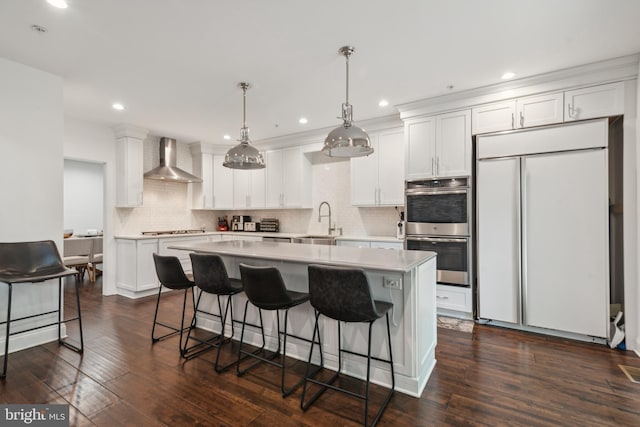 kitchen featuring white cabinets, wall chimney range hood, dark hardwood / wood-style floors, decorative light fixtures, and stainless steel appliances