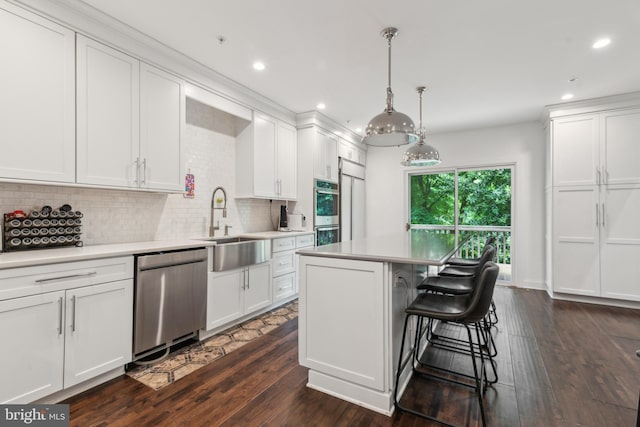 kitchen featuring appliances with stainless steel finishes, dark hardwood / wood-style flooring, a kitchen island, decorative light fixtures, and white cabinetry