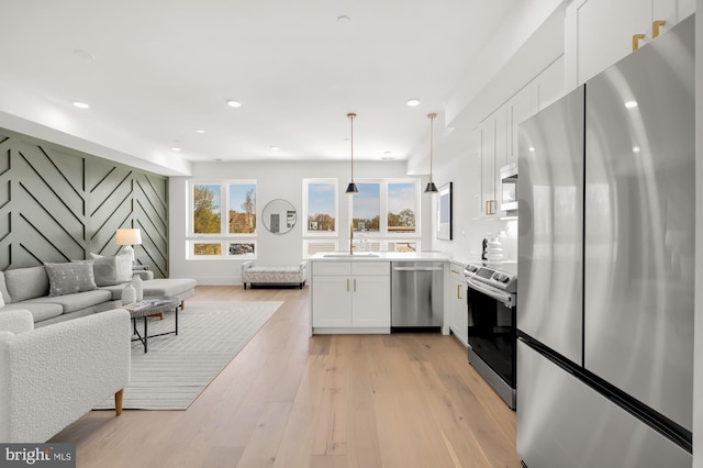 kitchen featuring white cabinets, hanging light fixtures, appliances with stainless steel finishes, light hardwood / wood-style floors, and kitchen peninsula