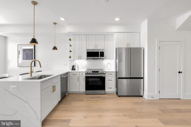 kitchen featuring white cabinetry, sink, kitchen peninsula, decorative light fixtures, and appliances with stainless steel finishes