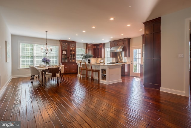 kitchen with a notable chandelier, hanging light fixtures, wall chimney exhaust hood, dark hardwood / wood-style floors, and a kitchen island