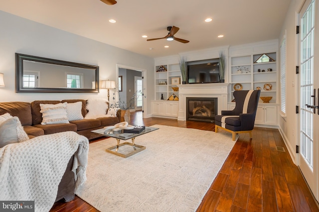 living room with plenty of natural light, dark hardwood / wood-style flooring, built in shelves, and ceiling fan