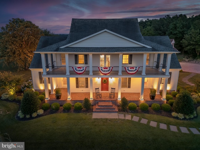 view of front of home featuring a balcony, a lawn, and covered porch