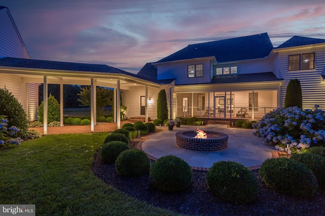 back house at dusk featuring a fire pit, a yard, and a patio area