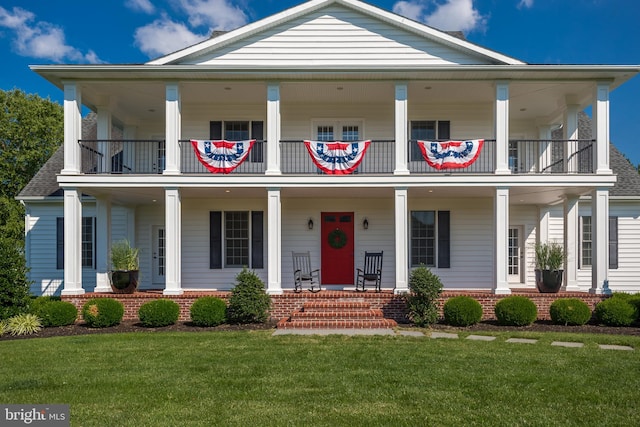 view of front of house with covered porch, a balcony, and a front lawn