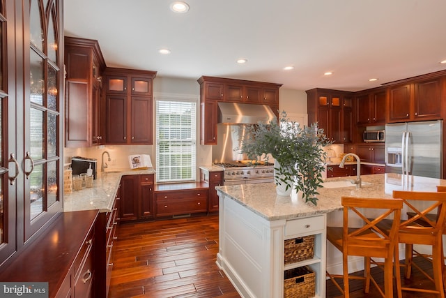 kitchen with wall chimney range hood, dark hardwood / wood-style flooring, stainless steel appliances, light stone countertops, and sink