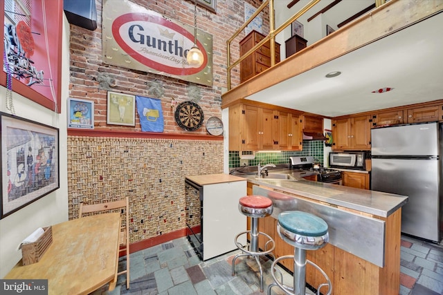 kitchen with brown cabinets, stone tile flooring, a high ceiling, appliances with stainless steel finishes, and brick wall