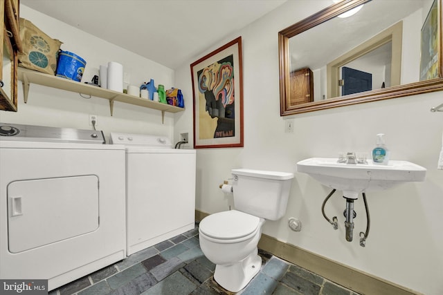 bathroom featuring toilet, washing machine and dryer, baseboards, and stone tile flooring