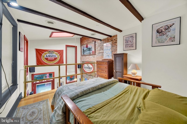 bedroom featuring beamed ceiling, wood finished floors, and brick wall