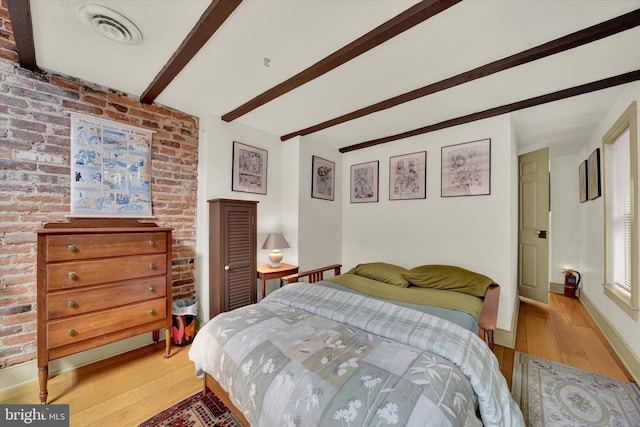 bedroom with light wood finished floors, visible vents, brick wall, baseboards, and beamed ceiling