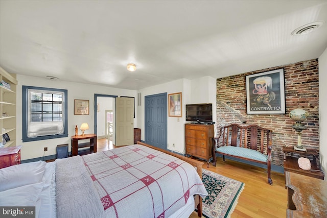 bedroom with visible vents, brick wall, baseboards, wood finished floors, and a closet