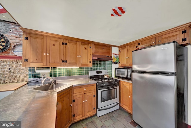 kitchen with a sink, under cabinet range hood, stainless steel counters, tasteful backsplash, and stainless steel appliances