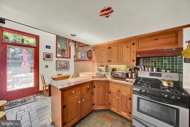 kitchen featuring stone tile floors, ventilation hood, stainless steel gas range, a peninsula, and light countertops