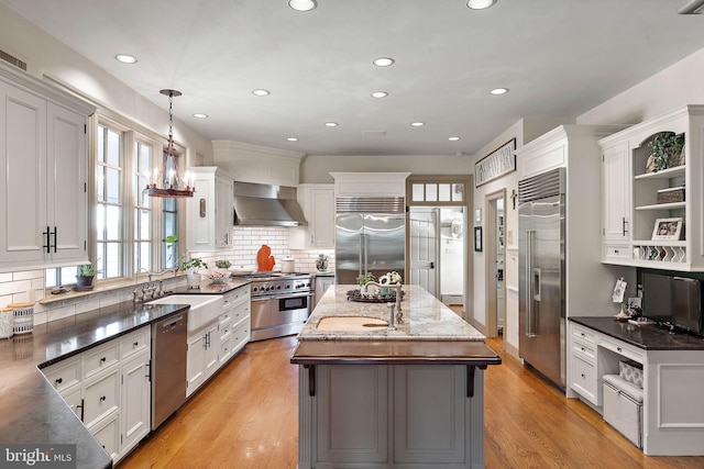 kitchen with wall chimney exhaust hood, hanging light fixtures, a kitchen island, high quality appliances, and white cabinets