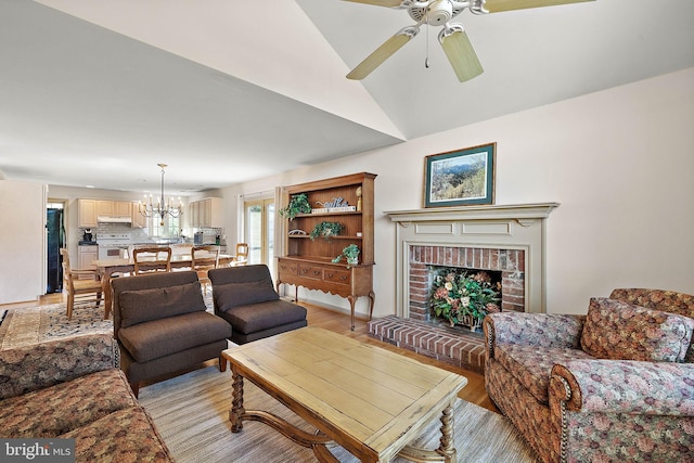 living room with ceiling fan with notable chandelier, vaulted ceiling, light hardwood / wood-style flooring, and a brick fireplace