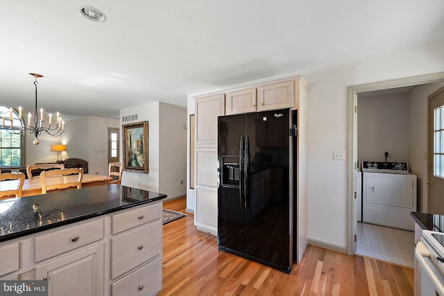 kitchen featuring black fridge, hanging light fixtures, washer and dryer, light wood-type flooring, and a notable chandelier