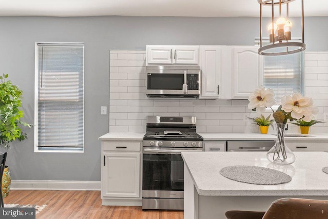 kitchen with light stone countertops, white cabinetry, stainless steel appliances, decorative light fixtures, and decorative backsplash