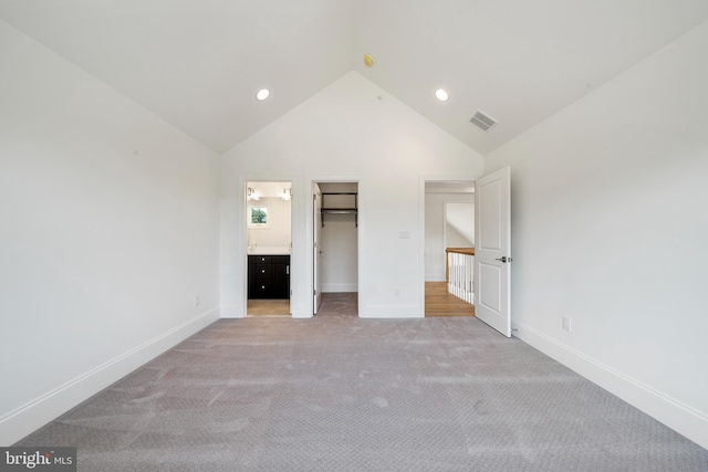 unfurnished bedroom featuring ensuite bathroom, vaulted ceiling, a spacious closet, light colored carpet, and a closet