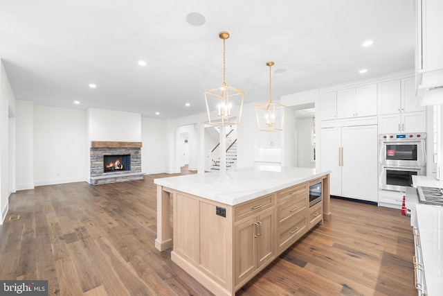 kitchen with pendant lighting, white cabinets, a stone fireplace, built in appliances, and a kitchen island