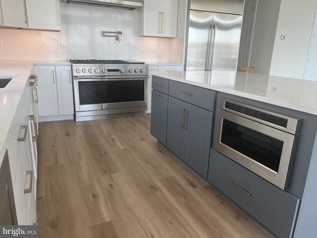 kitchen with built in appliances, light wood-style floors, white cabinets, light stone countertops, and tasteful backsplash