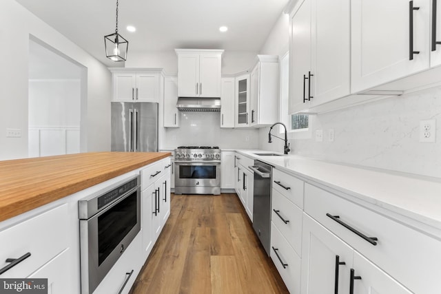 kitchen featuring decorative light fixtures, glass insert cabinets, white cabinetry, high quality appliances, and under cabinet range hood